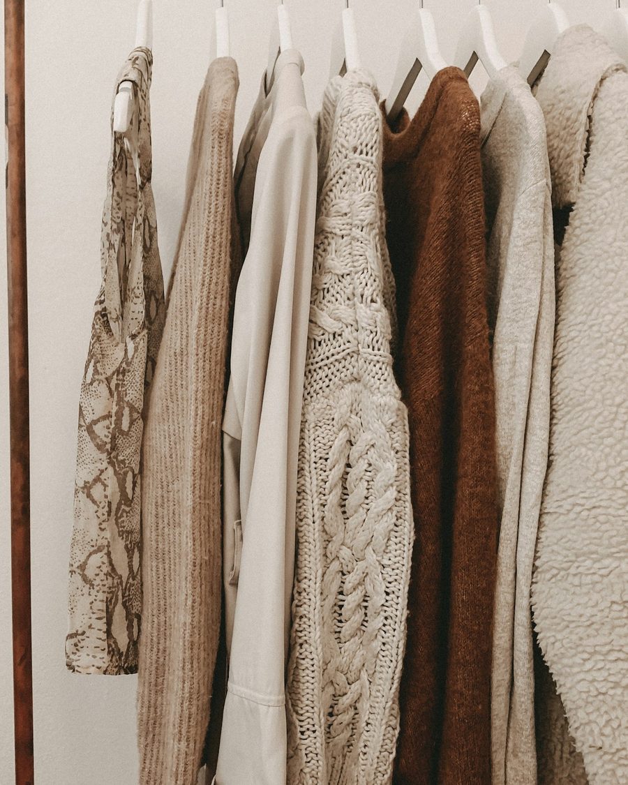 Kleiderstange mit Strickjacken und Pullovern in Creme, Beige und Braun, daneben getrocknetes Pampasgras