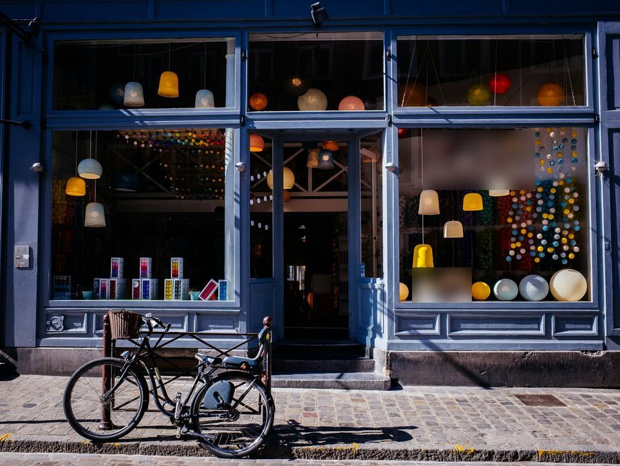 Blau gestrichene Ladenfront mit bunten Lampen im Schaufenster, davor ein Fahrrad mit Korb auf dem Kopfsteinpflaster